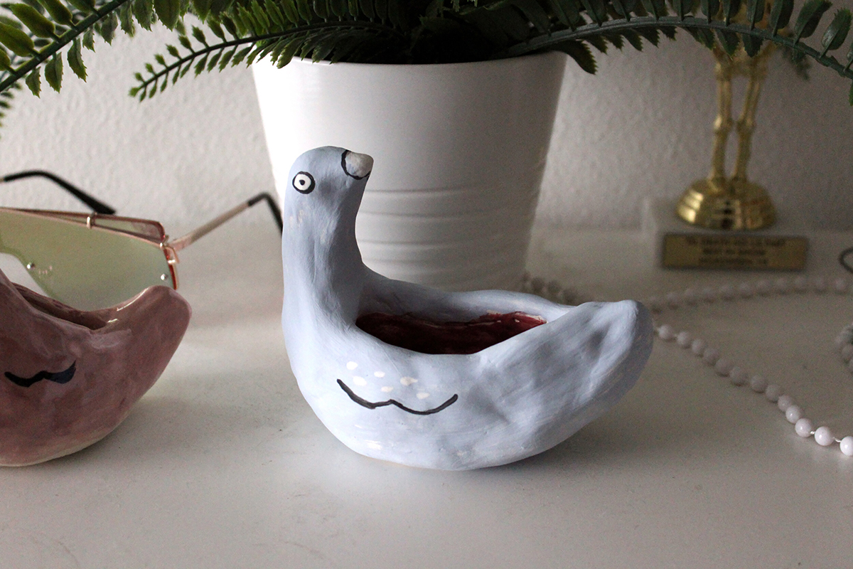Photograph of a table with some household items and a handbuilt and hand painted ceramic white pigeon bowl