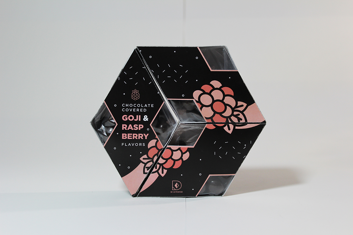Modular hexagonal packaging design, built from three diamond-shape chocolate boxes stacked together. Black art with modern pink and white confetti design with line art of raspberries, window in package shows chocolate.