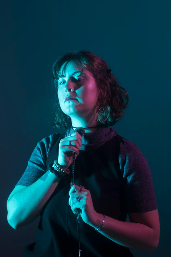 Image of Kali Wallner light using green and blue gels, she is staring off to the left and holding her bolo tie with both hands