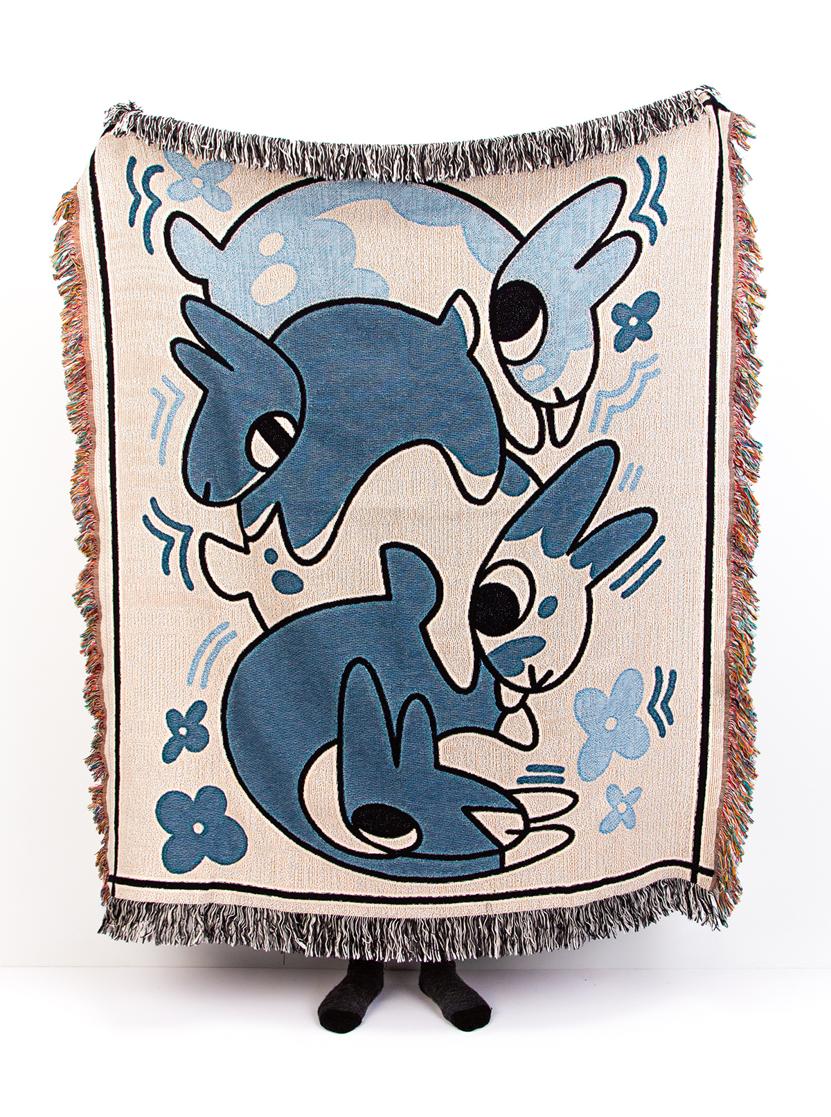 Lauren holds up a large throw quilt with an illustrated pattern of four stacked rabbits and flowers