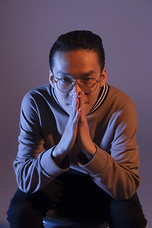 Trung crouched looking directly at the camera in front of him, hands pressed together in a 'please' or prayer gesture, resting against his nose.